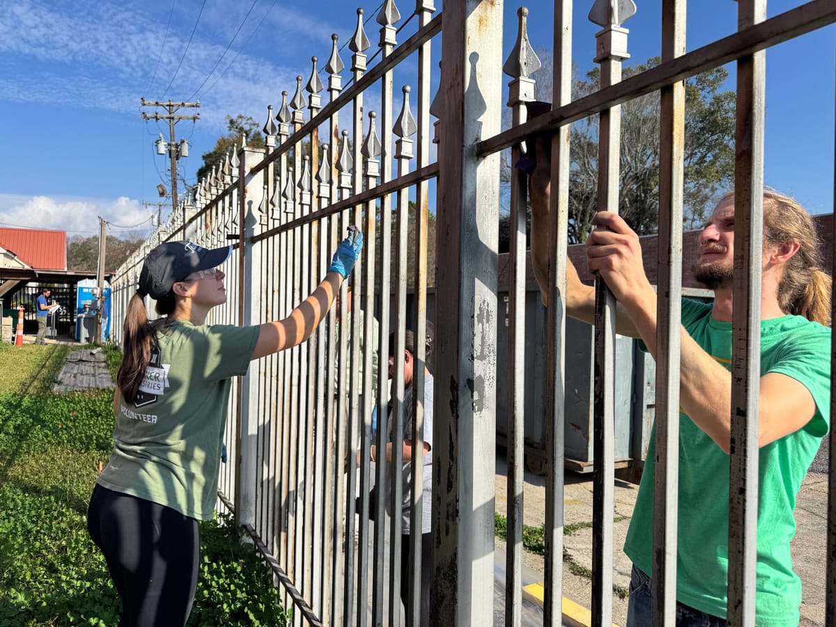 Volunteers prep a fence for painting in Mid City